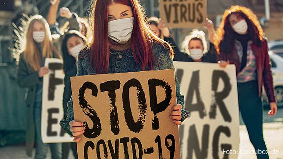 Auf einer Demonstration halten Frauen mit Minde-Nasen-Schutz Plakate mit der Aufschrift "Stop Covid-19"