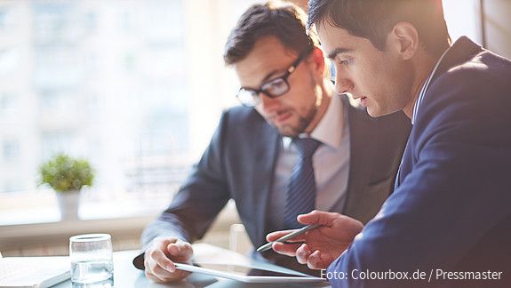 Zwei Männer im Büro sehen gemeinsam auf Tablet und besprechen sich