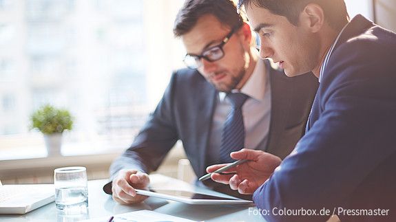 Zwei Männer im Büro sehen gemeinsam auf Tablet und besprechen sich