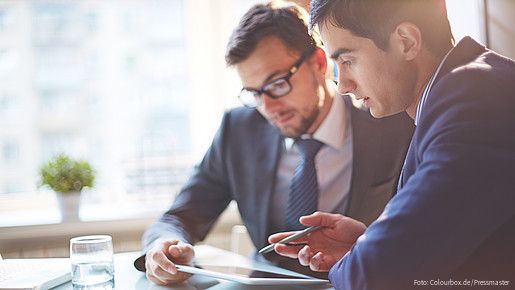 Zwei Männer im Büro sehen gemeinsam auf Tablet und besprechen sich