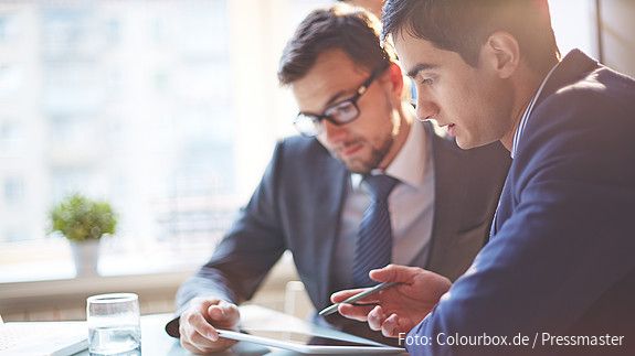 Zwei Männer im Büro sehen gemeinsam auf Tablet und besprechen sich