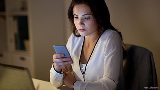 Eine junge Frau im Büro sieht mit ernstem Gesichtsausdruck auf das Display ihres Handys. 