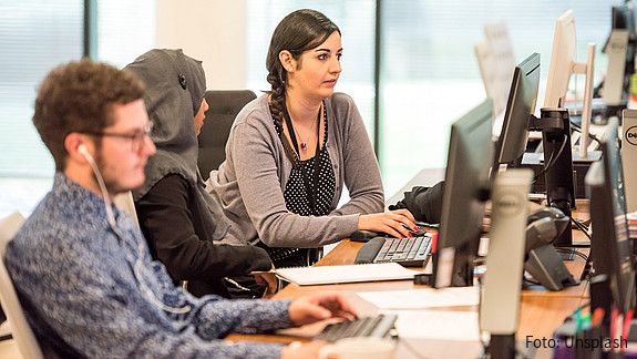 Blick in ein Büro auf einen jungen Mann und zwei Frauen, eine von ihnen trägt ein Kopftuch. Alle schauen auf ihre Computer-Bildschirme